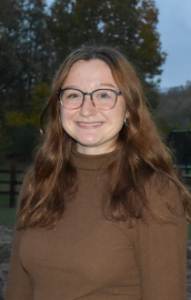 Image: Headshot of Jenna Steele, wearing brown shirt, light brown hair, with square glasses.